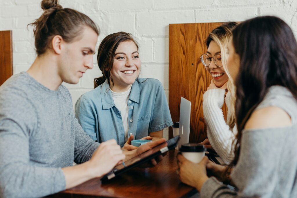 A candid moment of colleagues gathered around a table, chatting before a meeting begins. With coffee in hand and laptops open, the scene captures the informal conversations that naturally happen in the workplace. This image reflects connection, collaboration, and the everyday moments where relationships are built, often sparked by shared interests and pop culture.