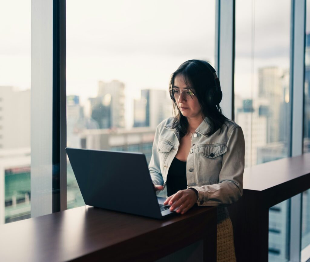 Focused professional working on a laptop in a modern office with city skyline views, representing productivity, remote work, and business focus.