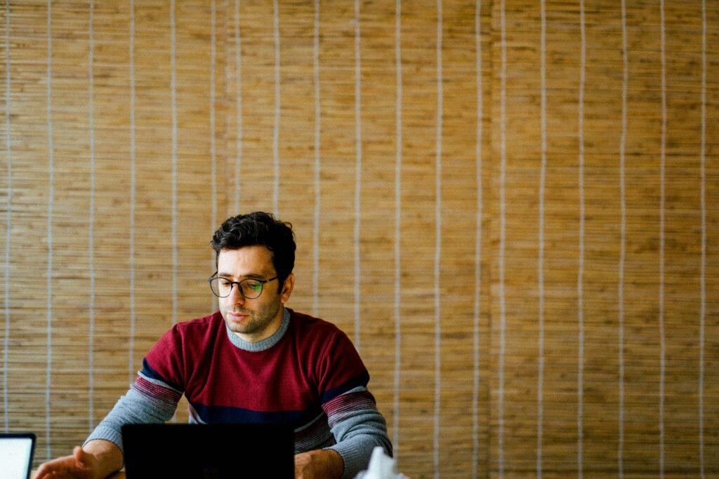 A person works quietly on a laptop in a modern office setting, with a warm wood-paneled wall in the background.